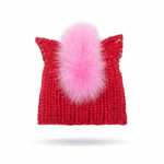 Red knitted hat with a pink faux fur pom-pom and silver hoops on a white background