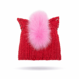 Red knitted hat with a pink faux fur pom-pom and silver hoops on a white background