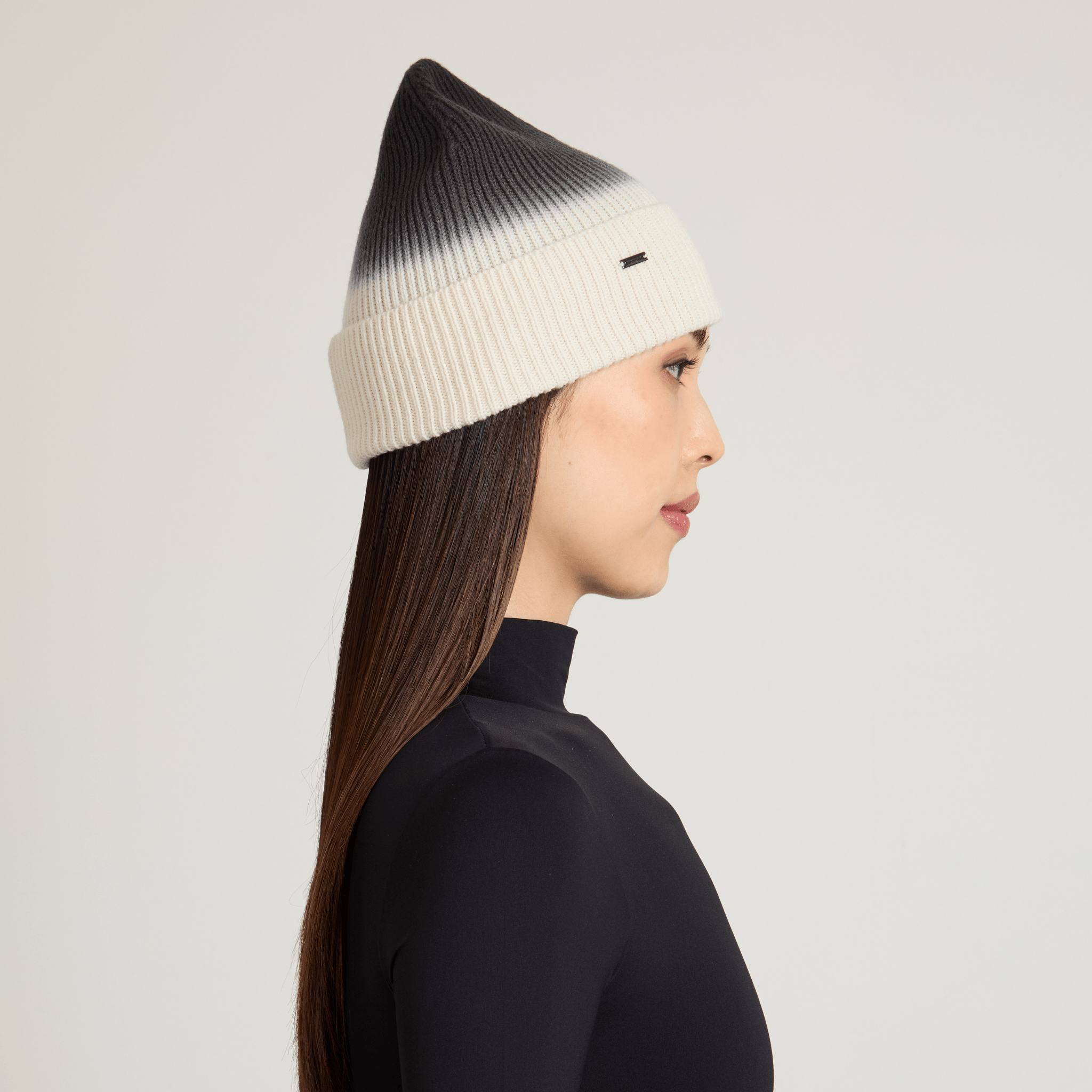 Woman wearing a black and white ombre beanie on a light gray background