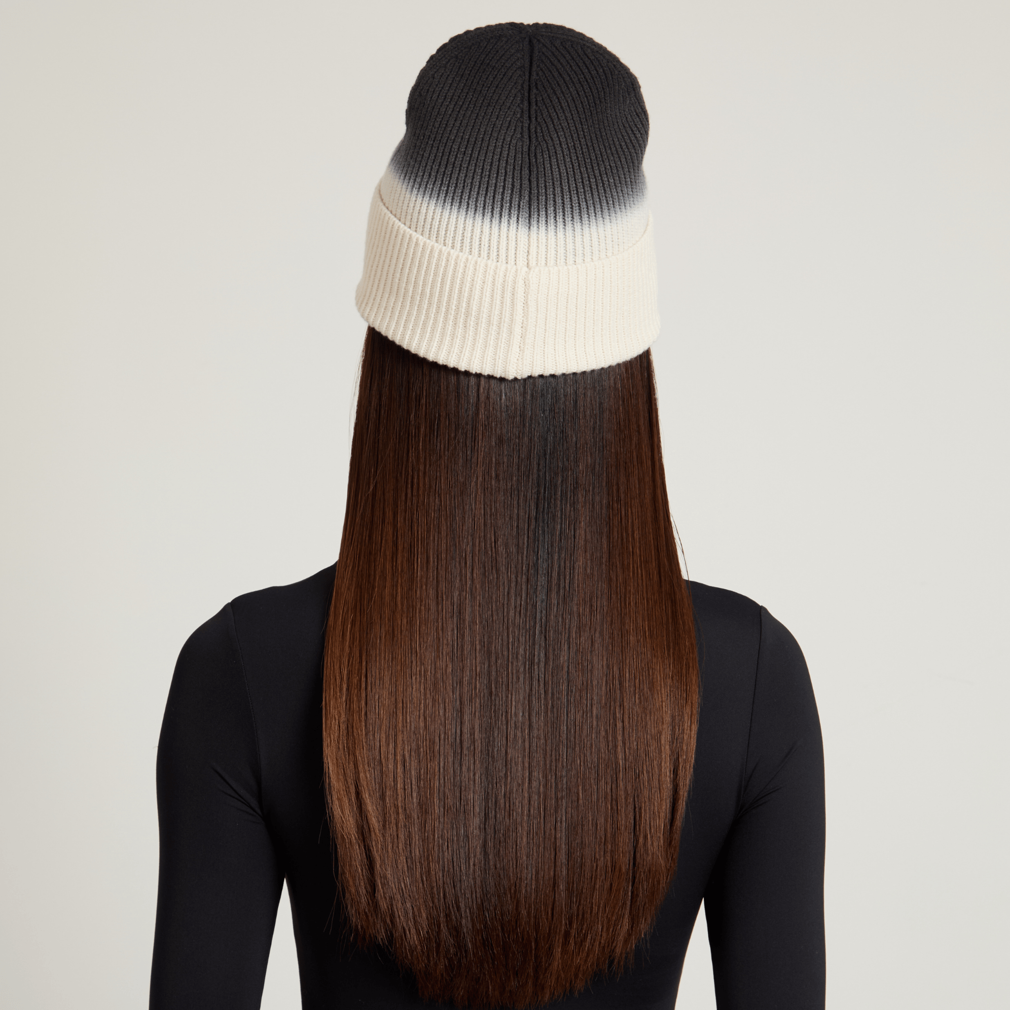 Back view of model wearing a black and white ombre beanie with long brown hair on a plain background