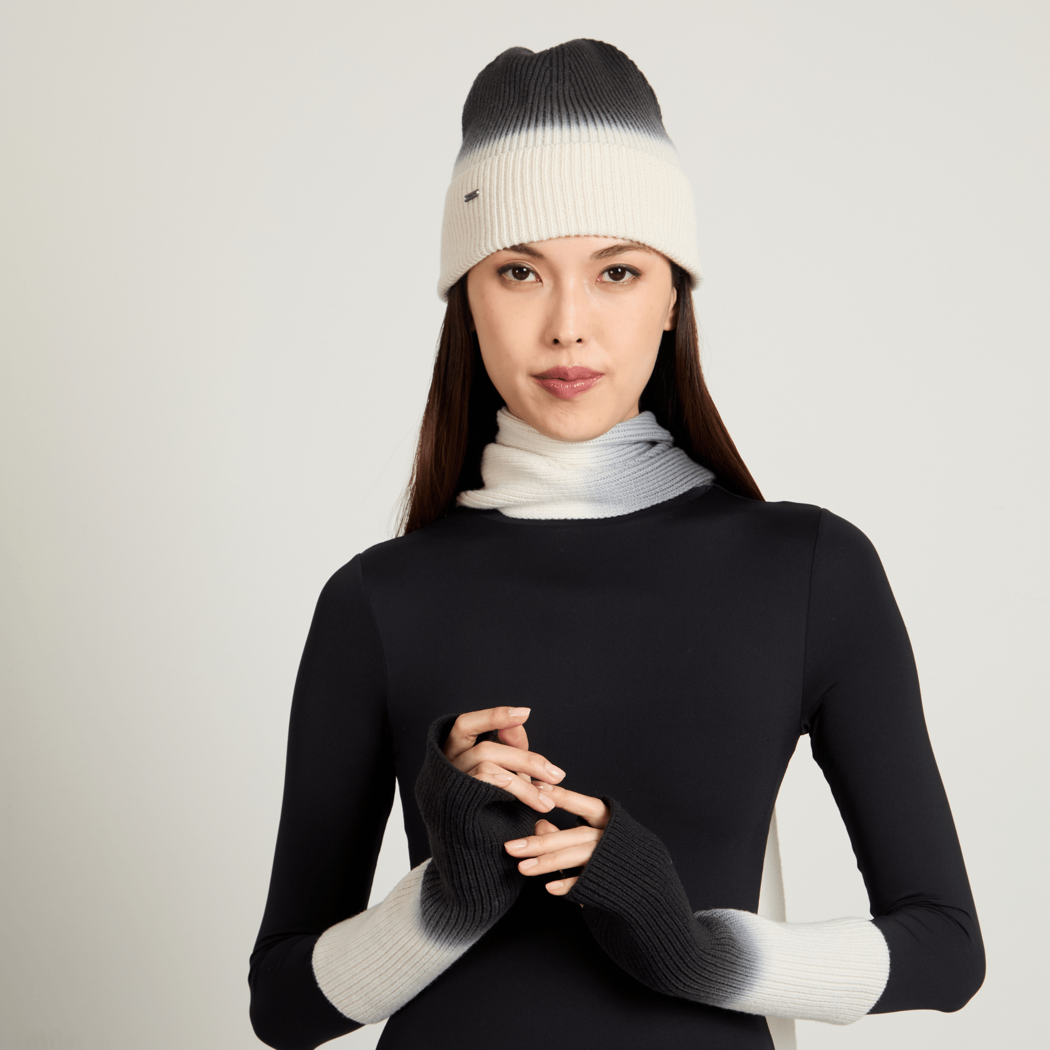 Model wearing a black and white ombre beanie, scarf, and gloves on a light gray background