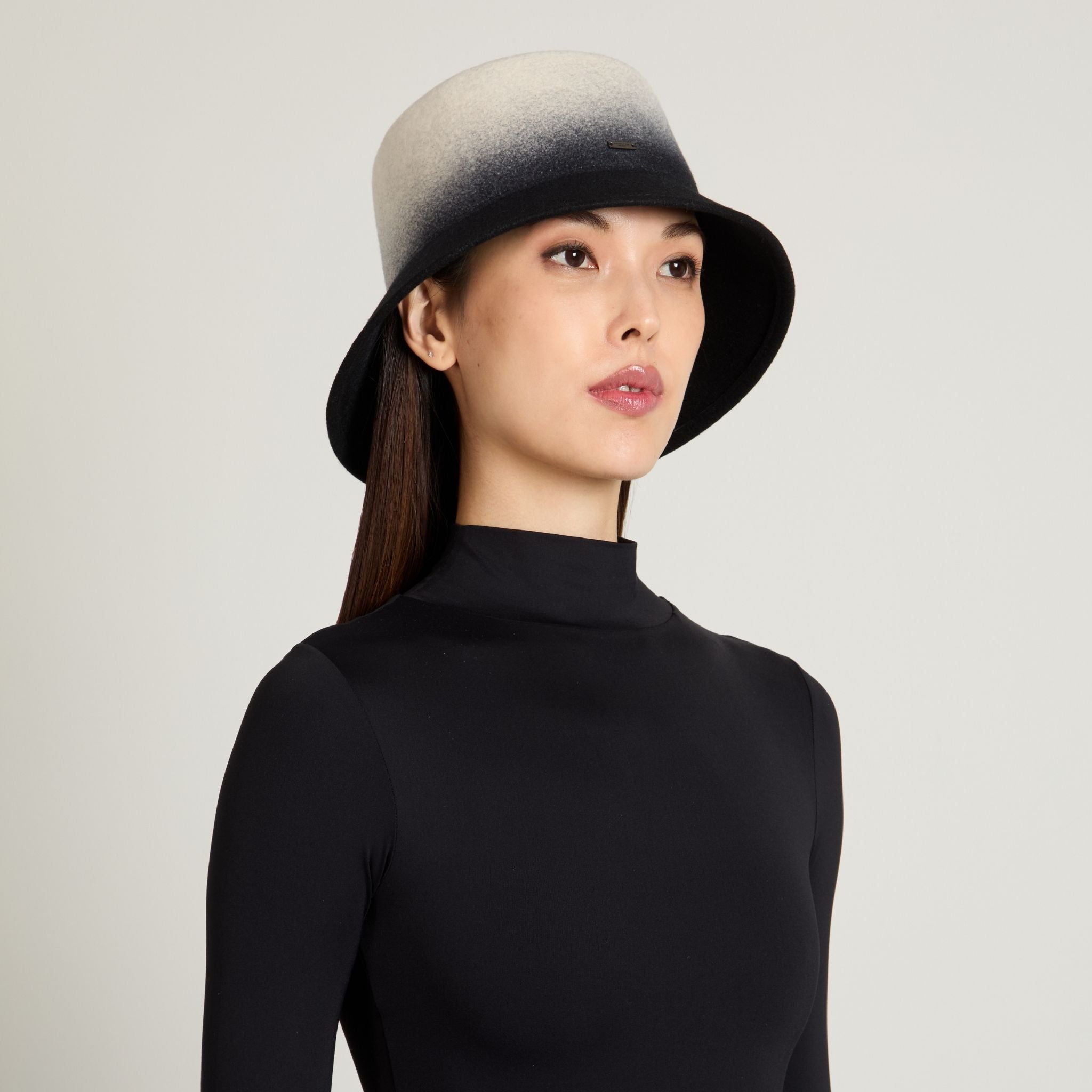 Woman wearing a black and gray gradient hat against a plain background