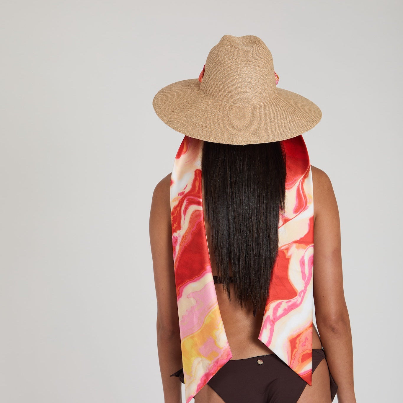 Person wearing a straw hat and colorful scarf with a plain background