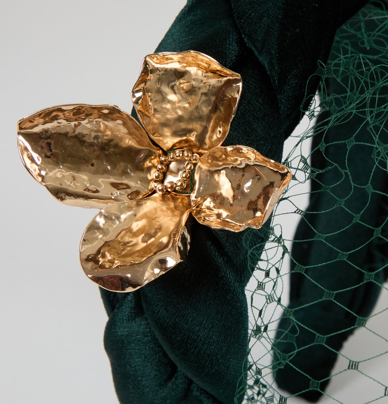 Detailed close-up showing a gold flower embellishment on the Grace headband, crafted in emerald panné velvet with a delicate veil