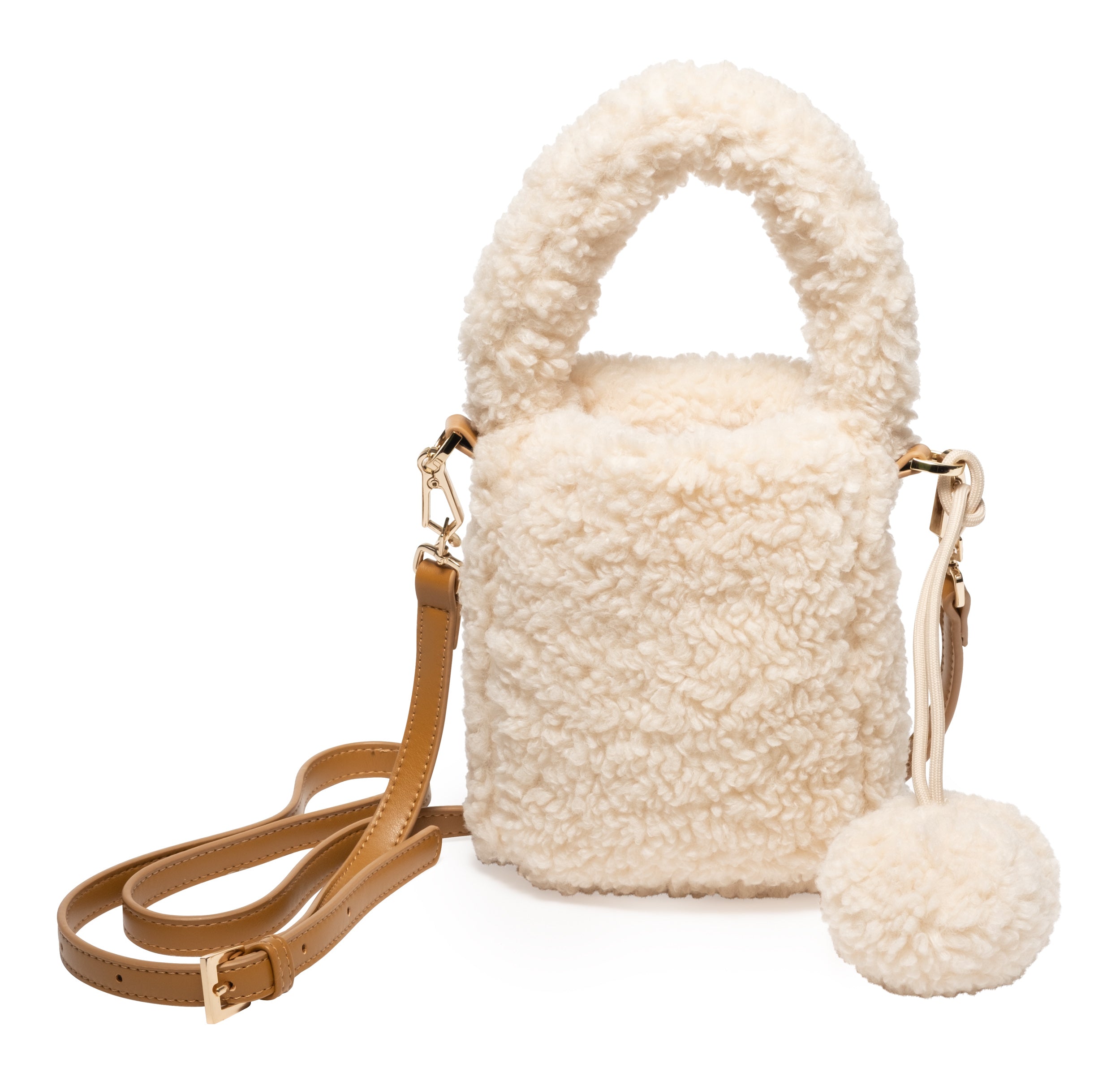 Eugenia Kim Tate Bag in Cream. A cozy faux shearling bucket bag featuring a plush handle, adjustable tan leather crossbody strap, and playful pom-pom detail. Perfect for adding warmth and texture to any winter outfit.